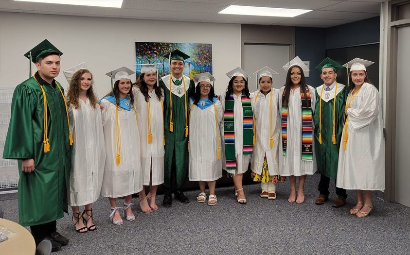 graduating seniors wearing white and green gowns for picture